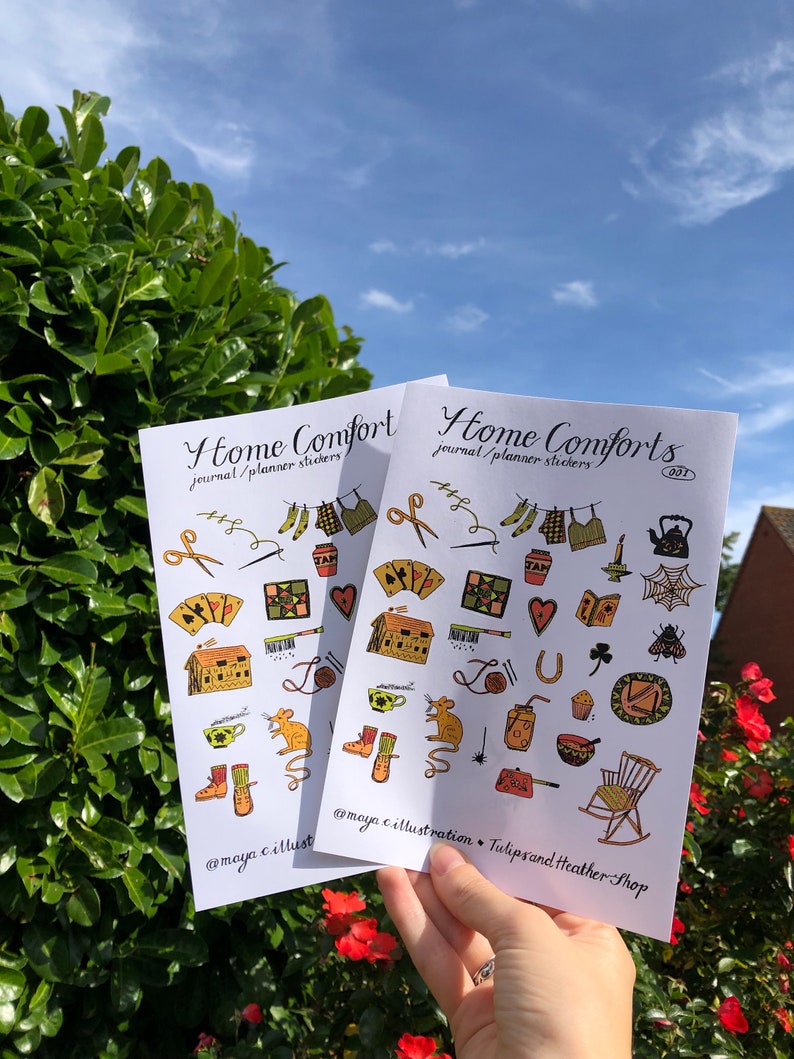 Puede incluir: Dos hojas de pegatinas con un tema hogare&ntilde;o. Las pegatinas presentan ilustraciones de una casa, una tetera, una mecedora, una telara&ntilde;a, un rat&oacute;n, una herradura, una taza de t&eacute;, una bota, una bola de lana, un coraz&oacute;n, un tr&eacute;bol, una abeja, una aguja de coser, un par de tijeras, un libro, una llave, un par de calcetines, una colcha, un frasco, un cupcake, una olla, una vela y una regadera. El texto en las pegatinas dice "Home Comforts journal/planner stickers 001" y "@maya.c.illust  TulipsandHeatherShop".