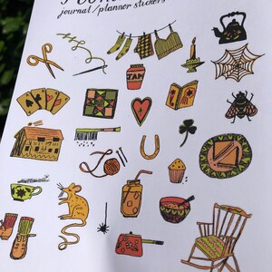 Puede incluir: Una hoja de pegatinas coloridas con un tema hogare&ntilde;o. Las pegatinas presentan ilustraciones de una tetera, una mecedora, una casa, una taza de t&eacute;, un tarro de mermelada, una mosca, una herradura, una bola de hilo, una vela, una telara&ntilde;a, un libro, un coraz&oacute;n, un tr&eacute;bol, una aguja de coser, un par de tijeras, un par de calcetines, una camisa, una colcha, una taza de t&eacute;, un rat&oacute;n, un frasco con una pajita, un taz&oacute;n de sopa, una cafetera y un par de botas. La hoja se titula "Home Comforts Journal/Planner Stickers 001".