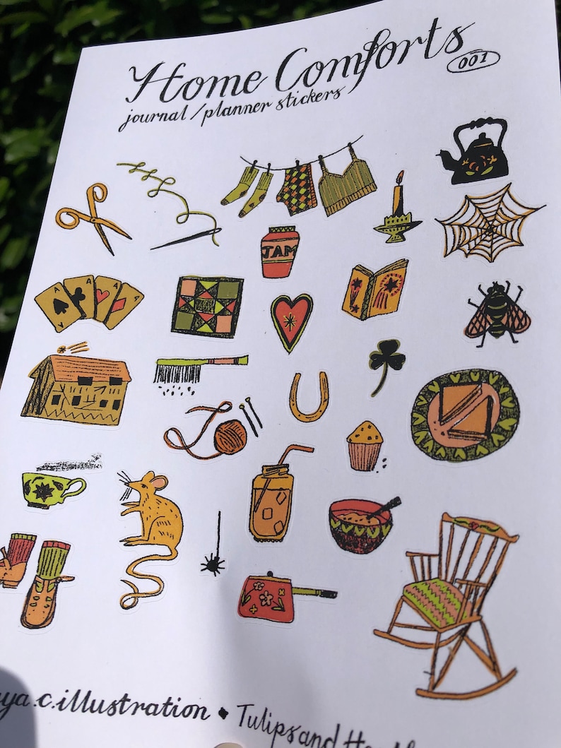 Puede incluir: Una hoja de pegatinas coloridas con un tema hogare&ntilde;o. Las pegatinas presentan ilustraciones de una tetera, una mecedora, una casa, una taza de t&eacute;, un tarro de mermelada, una mosca, una herradura, una bola de hilo, una vela, una telara&ntilde;a, un libro, un coraz&oacute;n, un tr&eacute;bol, una aguja de coser, un par de tijeras, un par de calcetines, una camisa, una colcha, una taza de t&eacute;, un rat&oacute;n, un frasco con una pajita, un taz&oacute;n de sopa, una cafetera y un par de botas. La hoja se titula "Home Comforts Journal/Planner Stickers 001".