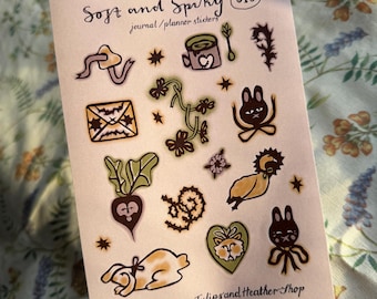 May include: A sheet of journal and planner stickers with the text "Soft and Spiky". The stickers feature whimsical illustrations of a mushroom, a teacup, a beet, a rabbit, and other botanical and animal designs in shades of brown, green, and yellow.