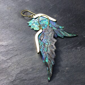 May include: A pair of iridescent abalone shell earrings with gold-toned metal accents. The earrings are shaped like wings and have a detailed, carved design.