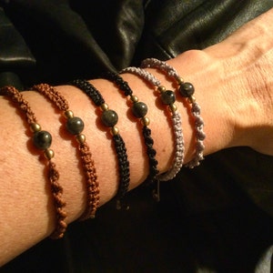 Puede incluir: Cinco pulseras trenzadas con cuentas grises oscuras y detalles dorados. Las pulseras se llevan en la muñeca.