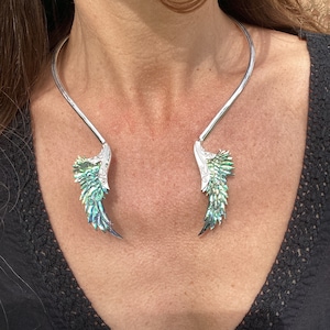 May include: A silver choker necklace with two wings on the ends. The wings are made of iridescent green and blue abalone shell.