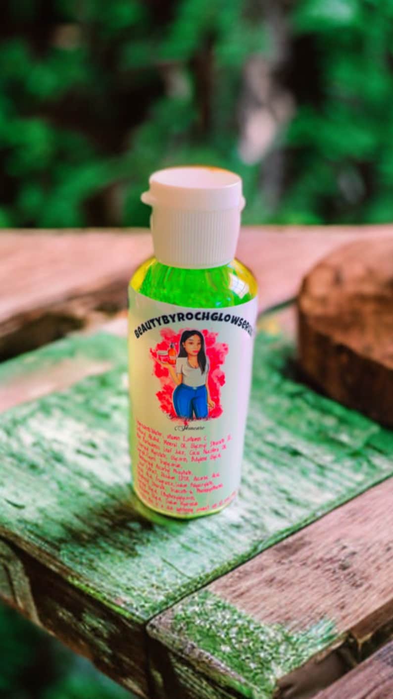 Puede incluir: Una botella transparente con una tapa blanca y un l&iacute;quido verde en su interior. La botella tiene una etiqueta con el texto "BEAUTYBYROCHGLOWSERUM" y una imagen de dibujos animados de una mujer. La etiqueta tambi&eacute;n enumera ingredientes como la vitamina C, el aloe vera y el &aacute;cido hialur&oacute;nico.