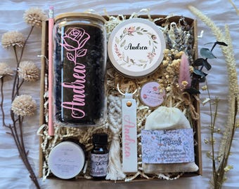 May include: A gift box containing a glass tumbler with a pink rose and the name Andrea, a candle with a floral wreath and the name Andrea, a macrame keychain with the name Andrea, a lip scrub, a small bottle, a hand cream, and a floral sachet.