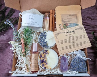 Puede incluir: Una caja de regalo llena de artículos calmantes, incluyendo velas de lavanda, cristales de amatista, lavanda seca y una botella de aceite esencial. La caja también incluye una pequeña bolsa de hierbas secas y una tarjeta con el texto "Calming" e información sobre los cristales.