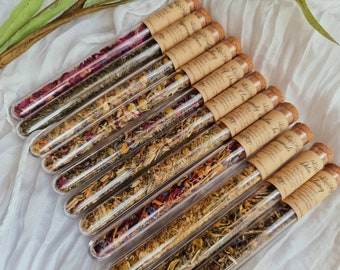 May include: A collection of ten glass test tubes filled with dried herbs and flowers. Each tube is topped with a cork stopper and has a label with handwritten text. The labels include names like "Sleepy Time", "A Dream", "Clarity", "Joy", "Lavender", and "Moon Magic".