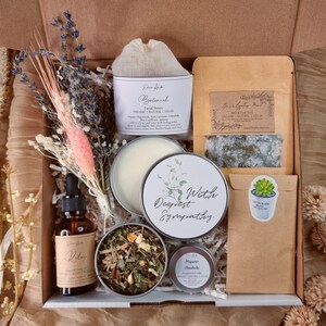 May include: A gift box filled with self-care items, including a candle, bath salts, tea, essential oil, and a small succulent. The box is decorated with dried flowers and a card that reads "With Deepest Sympathy".