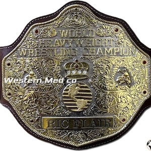 以下が含まれることがあります： 「WORLD HEAVY WEIGHT WRESTLING CHAMPION」と「RIC FLAIR」の文字が入った、金と銀のレスリングチャンピオンシップベルト。ベルトは茶色の革の裏地と複雑な花の模様が特徴です。