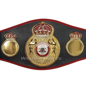 May include: A gold and black boxing championship belt with the words "World Boxing Association" and "WBA" on the front. The belt has two gold crowns on the sides and a larger gold crown on the front.