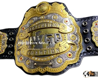 Pode incluir: Um cinturão de campeonato dourado e prateado com o texto "HEAVYWEIGHT CHAMPION" e "WGP CHAMPION". O cinturão tem uma correia de couro preta e é decorado com joias vermelhas e desenhos intrincados. O nome "KAZUCHIKA OKADA" também é visível.
