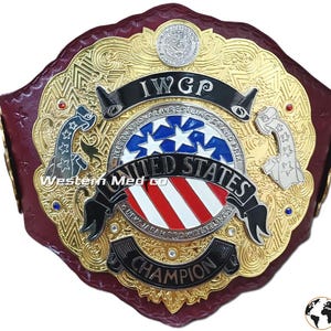 Könnte beinhalten: Ein gold- und roter Wrestling-Meisterschaftsgürtel mit der Aufschrift "IWGP United States Champion". Der Gürtel hat ein rotes Lederband und eine goldene Metallplatte mit einem rot-weiß-blauen amerikanischen Flaggenmuster.