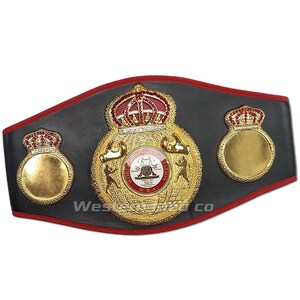 May include: A black and gold boxing championship belt with red accents. The belt features a large central emblem with the words "World Boxing Association" and "WBA" in gold lettering. The emblem also includes a crown, two boxing gloves, and a globe. The belt has two smaller crowns on either side of the central emblem.