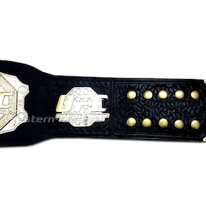 Pu&ograve; includere: Una cintura da campione UFC in pelle nera con dettagli dorati e argentati. La cintura presenta il logo UFC e le parole "Ultimate Fighting Championship".