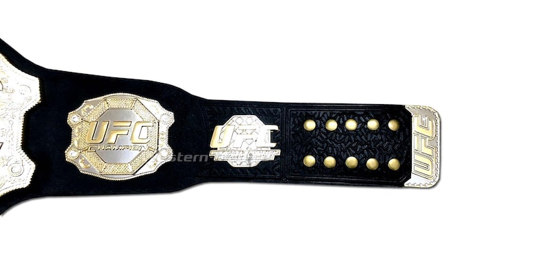 Pu&ograve; includere: Una cintura da campione UFC in pelle nera con dettagli dorati e argentati. La cintura presenta il logo UFC e le parole "Ultimate Fighting Championship".