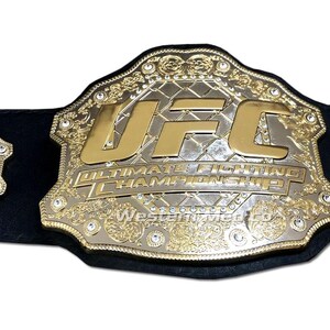 Pu&ograve; includere: Una cintura da campione UFC dorata con un cinturino in pelle nera. La cintura presenta un grande logo UFC dorato e le parole "Ultimate Fighting Championship".