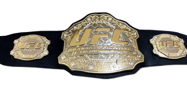 Pu&ograve; includere: Una cintura da campione UFC dorata con un cinturino in pelle nera. La cintura presenta un grande logo UFC dorato e le parole "Ultimate Fighting Championship".