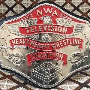 May include: A silver and red wrestling championship belt with the text "NWA Television Heavyweight Wrestling Champion" and a stylized eagle design.