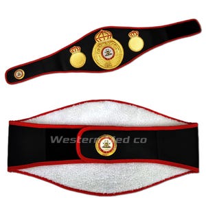 May include: A black boxing championship belt with gold accents and a large central emblem featuring a crown and the words "World Boxing Council". The belt is shown in two positions, one with the buckle facing the viewer and the other with the inside of the belt facing the viewer.