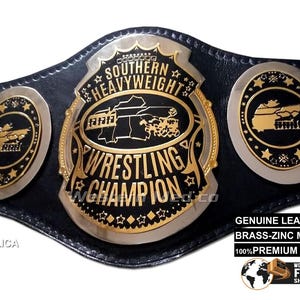 Puede incluir: Un cinturón de campeonato de lucha libre de réplica con una correa de cuero negro y placas de metal doradas y plateadas. La placa central presenta el texto "Southern Heavyweight Wrestling Champion" con un mapa en blanco y negro de un estado. Las placas laterales presentan una imagen en blanco y negro de un estado con estrellas alrededor del borde.