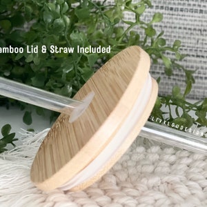May include: A close-up of a bamboo lid and clear straw. The lid is light brown with a white rim and a hole for the straw. The text "Bamboo Lid & Straw Included" is visible in the image.