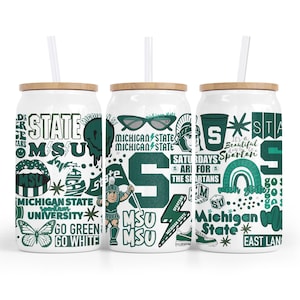 May include: Three white glass tumblers with bamboo lids and straws. Each tumbler has a different design with green and white graphics, including the text "MSU", "Michigan State", and Spartan-themed illustrations. The tumblers are designed for cold drinks.