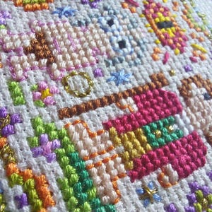 May include: Close-up of a colorful cross-stitch embroidery with various geometric shapes and patterns in shades of pink, orange, green, blue, and gold.