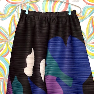 May include: Black pleated skirt with a colorful abstract print featuring shades of blue, green, purple, and white.