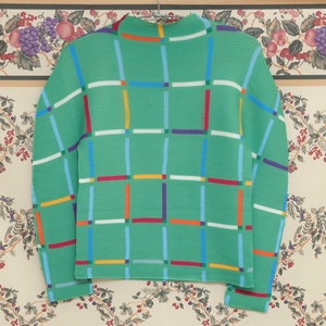 May include: A green sweater with a geometric pattern of colourful stripes. The sweater has a high neck and long sleeves.