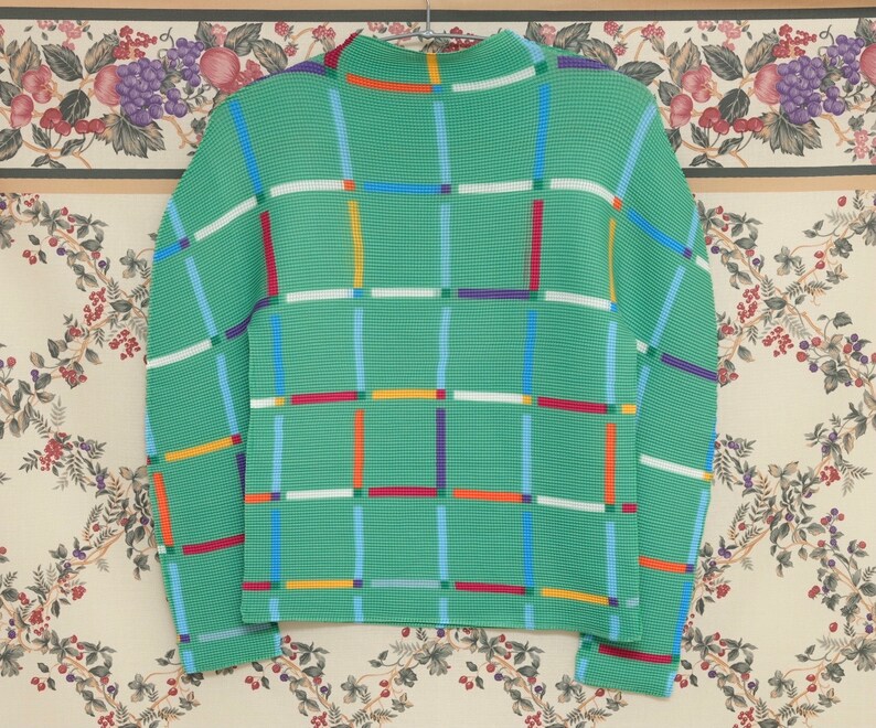 May include: A green sweater with a geometric pattern of colourful stripes. The sweater has a high neck and long sleeves.