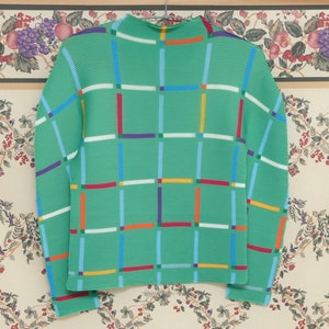 May include: A green sweater with a geometric pattern of colourful lines. The sweater has a high neck and long sleeves.