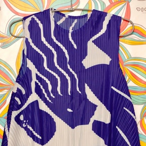 May include: A sleeveless, pleated dress with a white and purple abstract pattern. The dress is made of a lightweight, flowing fabric.