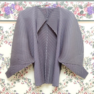 Op de afbeelding: Een grijze geplooide cardigan met een uniek open rugontwerp. De cardigan heeft lange mouwen en een ontspannen pasvorm.