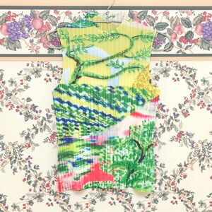May include: A sleeveless, yellow, green, blue, and pink pleated top with an abstract print. The top has a high neck and a relaxed fit.