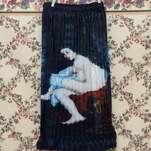 Peut inclure: Une jupe plissée noire avec une image imprimée d'une femme en robe bleue assise dans une piscine d'eau. La jupe a un ourlet en zigzag.