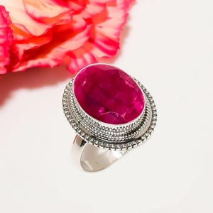 May include: A silver ring with a large, oval-shaped, pink gemstone set in a decorative silver bezel. The ring has a wide band.