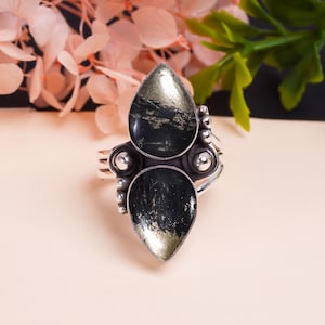 May include: A silver ring with two teardrop-shaped black and gold stones. The stones are set in a silver band with small silver beads.