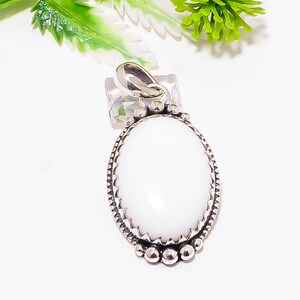 Puede incluir: Colgante ovalado de piedra preciosa blanca con un engaste de metal plateado. El colgante tiene un borde texturizado y un lazo para una cadena. La piedra preciosa es lisa y pulida. Es una joya.