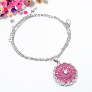 Könnte beinhalten: Eine silberfarbene Halskette mit einem runden Anhänger, der mit mehreren tropfenförmigen rosa Steinen in einem Blumenmuster besetzt ist, in der Mitte einen klaren Stein trägt und von kleinen klaren Steinen umrandet wird.