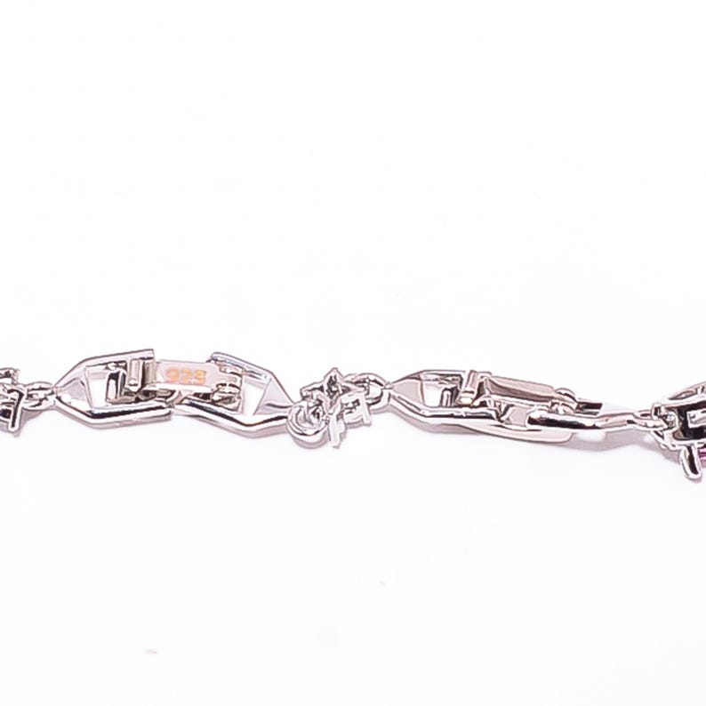 Pode incluir: Uma vista de perto de uma pulseira de corrente prateada com um design de elos &uacute;nico. A pulseira apresenta um fecho e v&aacute;rios elementos decorativos. O fundo branco liso real&ccedil;a os detalhes da joia.