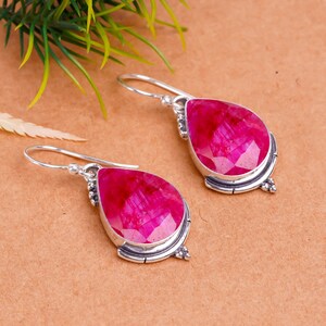 Puede incluir: Un par de pendientes de plata con piedras preciosas de rubí rosa. Los pendientes tienen forma de lágrima y están adornados con detalles plateados.