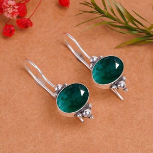 Può includere: Un paio di orecchini pendenti in argento con pietre ovali verdi. Gli orecchini hanno un design semplice con un piccolo dettaglio di perline d'argento.