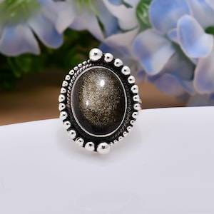 Può includere: Un anello d'argento con una grande pietra ovale di orolite incastonata in una ghiera a perline.