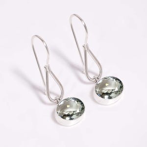 May include: A pair of silver dangle earrings with green gemstone drops. The earrings have a simple, elegant design.
