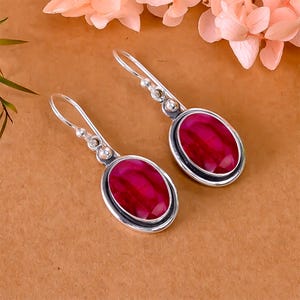 May include: A pair of silver earrings with oval-shaped red gemstones. The earrings have a simple design with a small silver bead on the top of the gemstone.