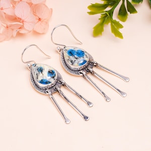 Può includere: Un paio di orecchini pendenti in argento con gocce di pietre preziose blu e bianche. Ogni orecchino ha tre fili d'argento che pendono dal basso.