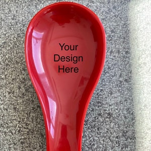 May include: A red ceramic spoon rest with the text "Your Design Here" printed on the front.