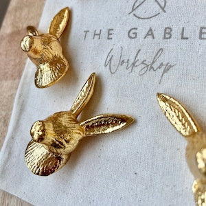 May include: A set of gold rabbit-shaped drawer pulls. The pulls are displayed on a white fabric surface with the text "THE GABLE Workshop" printed on it.