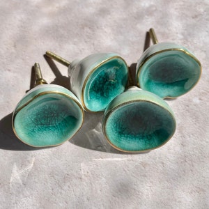 May include: Four ceramic cabinet knobs with a teal blue glaze and gold trim. The knobs have a rounded, organic shape.