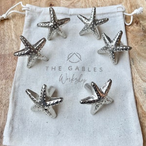 May include: Six silver starfish drawer pulls in a white fabric bag. The bag has the text "The Gables Workshop" printed on it.
